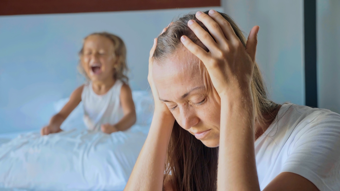 Upset mother with angry little child screaming pillow on the background