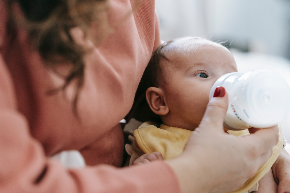 Crop mother feeding infant with milk from bottle